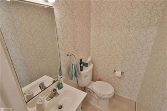 bathroom with toilet, wallpapered walls, and a sink