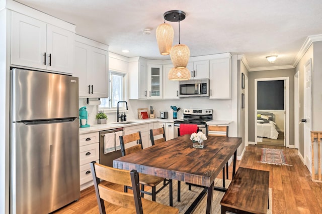 kitchen featuring a sink, light countertops, appliances with stainless steel finishes, white cabinetry, and crown molding