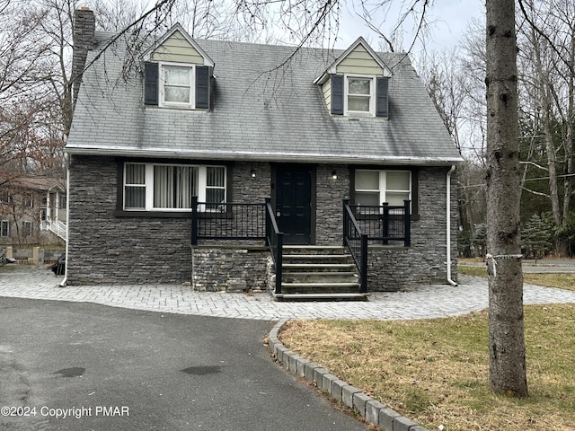 new england style home with stone siding and a chimney