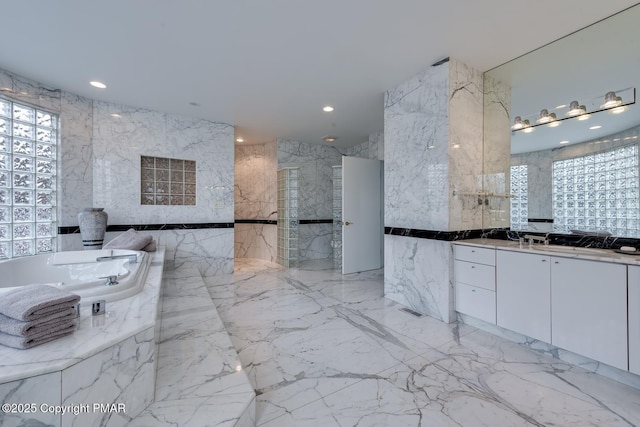 bathroom with a bath, stone wall, vanity, and tile walls