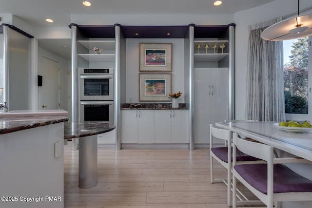 kitchen with light wood-style flooring, dark stone countertops, white cabinets, and stainless steel double oven