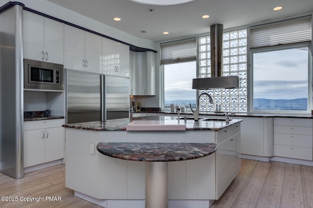 kitchen with built in appliances, plenty of natural light, a center island with sink, and white cabinetry