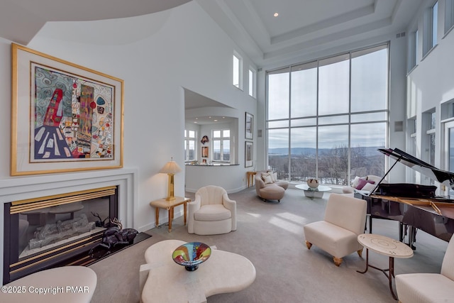 carpeted living room with baseboards, arched walkways, a glass covered fireplace, a towering ceiling, and a mountain view