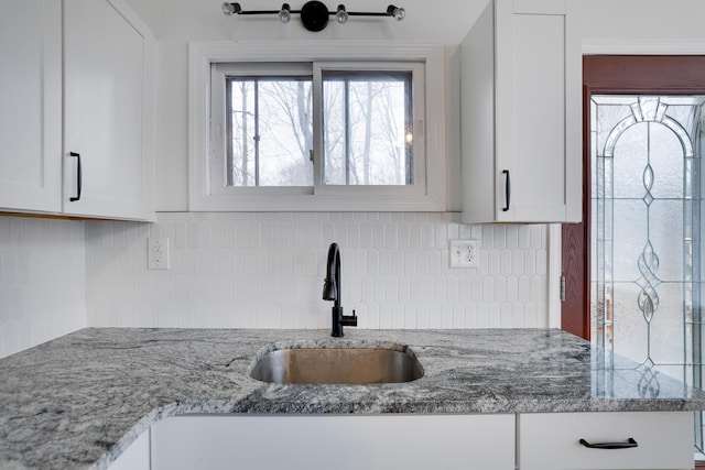 kitchen with a sink, decorative backsplash, light stone counters, and white cabinets