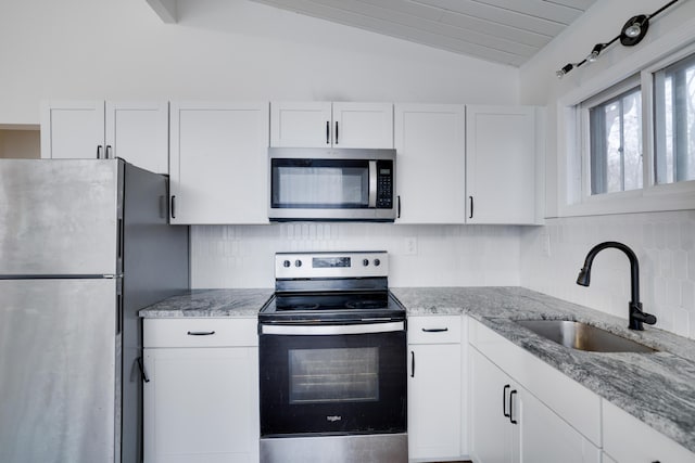 kitchen featuring light stone countertops, lofted ceiling, decorative backsplash, appliances with stainless steel finishes, and a sink