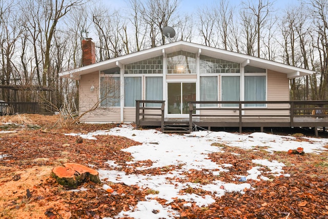 view of front of property with a wooden deck, a sunroom, and a chimney