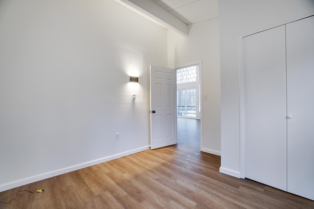 unfurnished bedroom featuring baseboards, beam ceiling, wood finished floors, and a towering ceiling