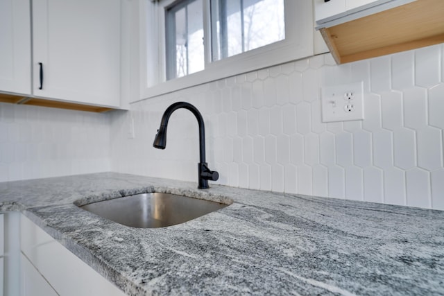 interior details with tasteful backsplash, white cabinets, light stone countertops, and a sink