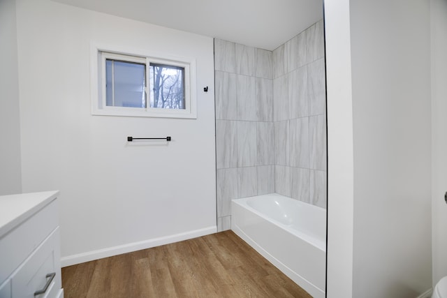 bathroom with washtub / shower combination, baseboards, wood finished floors, and vanity