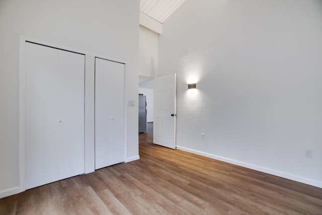 unfurnished bedroom featuring light wood finished floors, baseboards, multiple closets, a high ceiling, and freestanding refrigerator