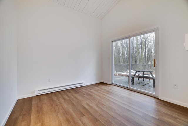 spare room featuring a baseboard heating unit, lofted ceiling, wood finished floors, and baseboards