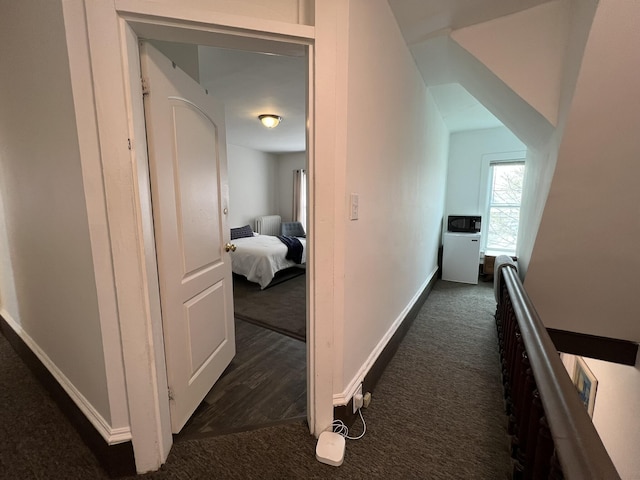 hallway featuring dark colored carpet and baseboards
