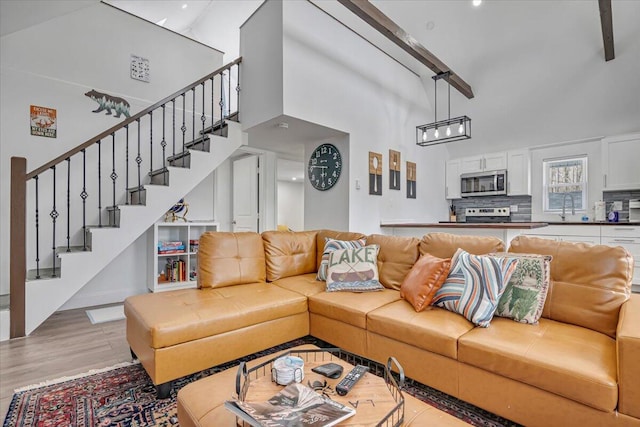 living room featuring stairway, light wood-style flooring, and a towering ceiling