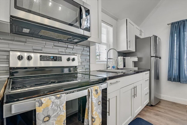 kitchen featuring light wood finished floors, a sink, stainless steel appliances, white cabinets, and tasteful backsplash