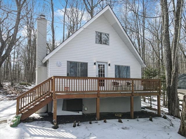 snow covered house featuring a deck, stairway, and a chimney