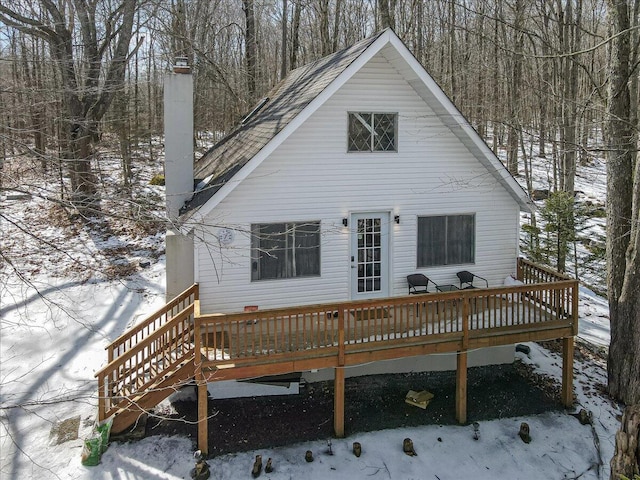 snow covered rear of property with a wooden deck and a chimney