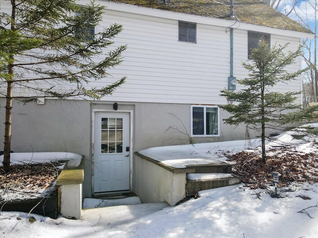 snow covered property entrance with a shingled roof