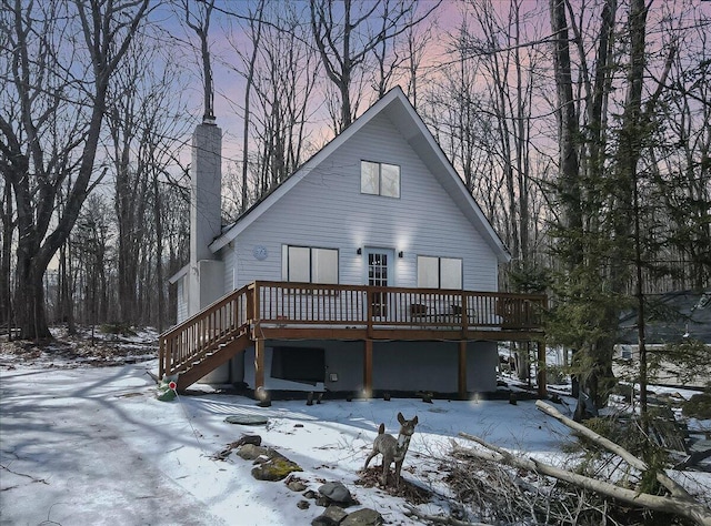 snow covered back of property with stairs, a deck, and a chimney