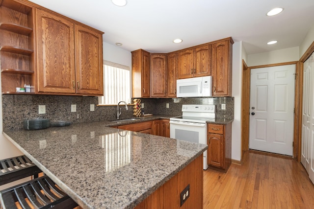 kitchen featuring a sink, a peninsula, stone counters, white appliances, and brown cabinetry