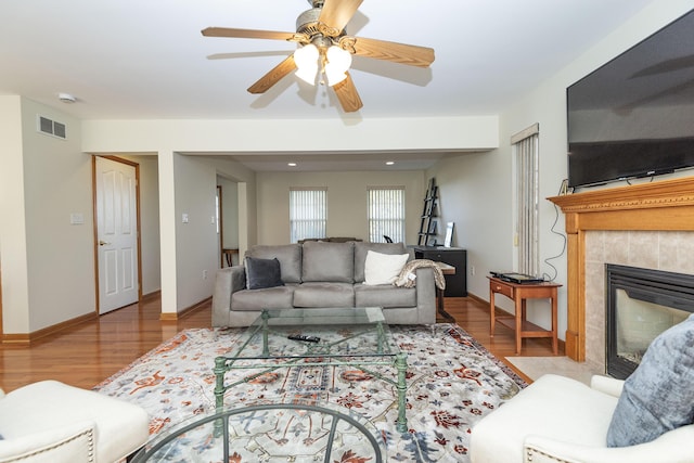 living room featuring a tiled fireplace, wood finished floors, ceiling fan, baseboards, and visible vents