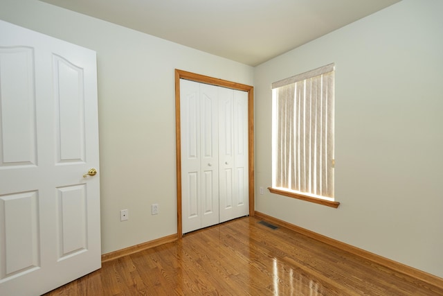 unfurnished bedroom with a closet, visible vents, wood finished floors, and baseboards