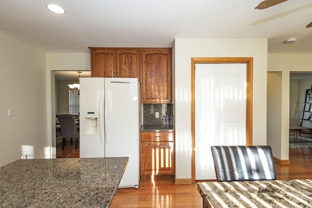kitchen with white refrigerator with ice dispenser, tasteful backsplash, light wood finished floors, and brown cabinetry