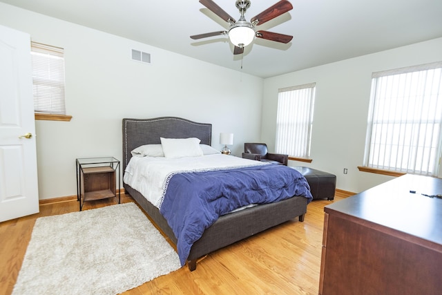 bedroom with light wood finished floors, visible vents, ceiling fan, and baseboards