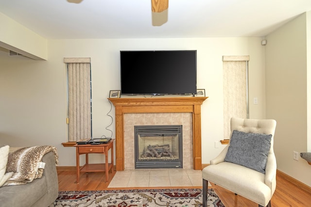 living area with a tile fireplace, a ceiling fan, wood finished floors, and baseboards