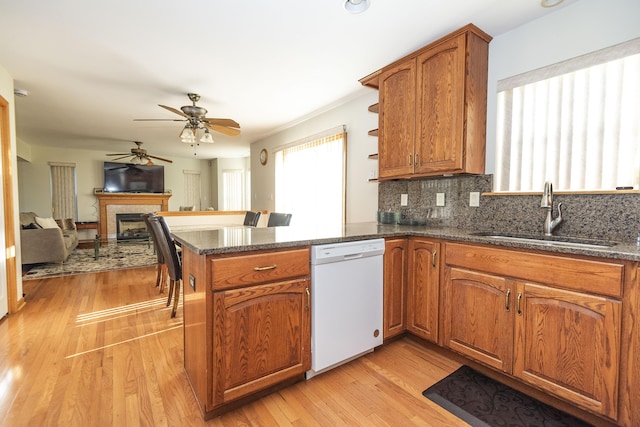 kitchen featuring brown cabinets, dishwasher, a fireplace, a sink, and a ceiling fan