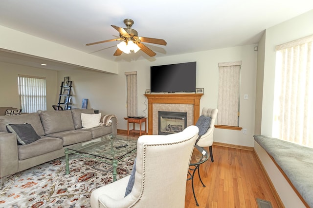living area with light wood finished floors, a tile fireplace, a ceiling fan, visible vents, and baseboards