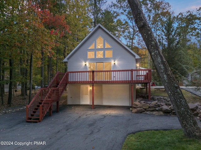 rear view of house featuring a garage, driveway, a wooden deck, and stairs