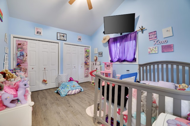 bedroom with ceiling fan, wood finished floors, vaulted ceiling, and two closets