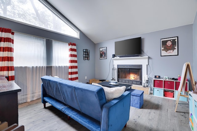 living room featuring vaulted ceiling, a lit fireplace, and wood finished floors