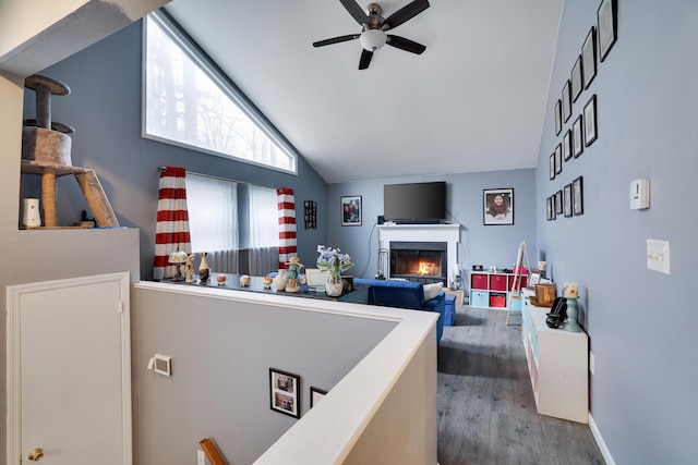 interior space featuring a warm lit fireplace, a ceiling fan, vaulted ceiling, and wood finished floors