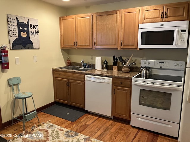 kitchen featuring white appliances, wood finished floors, a sink, baseboards, and brown cabinetry