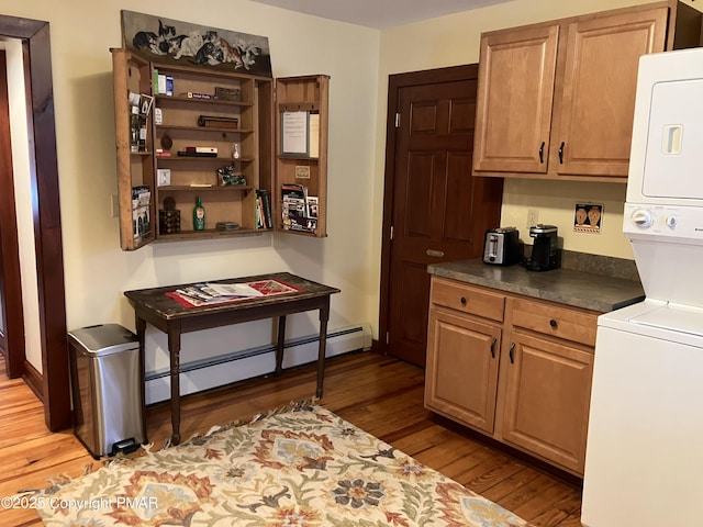 kitchen featuring a baseboard heating unit, stacked washer / dryer, light wood-style floors, and dark countertops