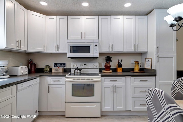 kitchen with white appliances, dark countertops, recessed lighting, and white cabinets