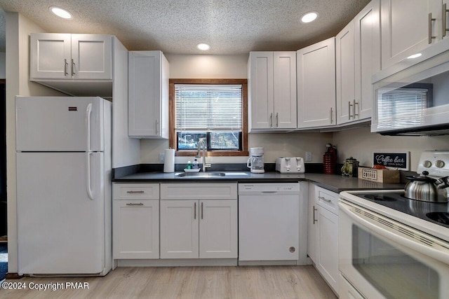 kitchen with dark countertops, light wood-style floors, a sink, a textured ceiling, and white appliances