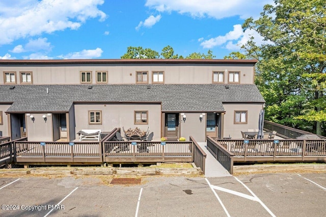 view of property with uncovered parking, roof with shingles, and a wooden deck