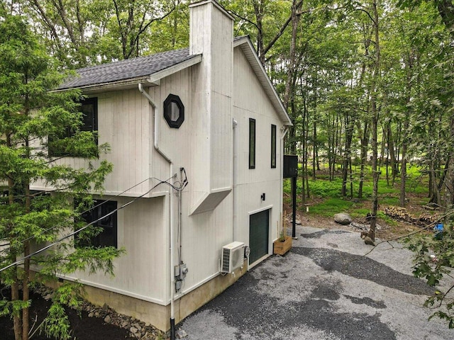 754 Clubhouse Dr, East Stroudsburg, PA 18302 - view of home's exterior featuring an attached garage, roof with shingles, a chimney, asphalt driveway, and view of scattered trees