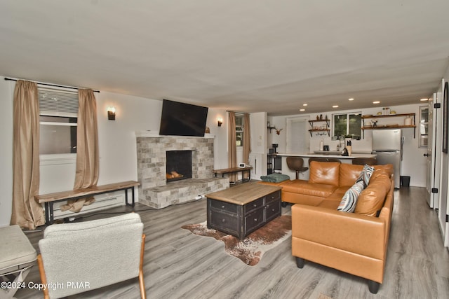 living area with light wood-type flooring, a stone fireplace, and recessed lighting