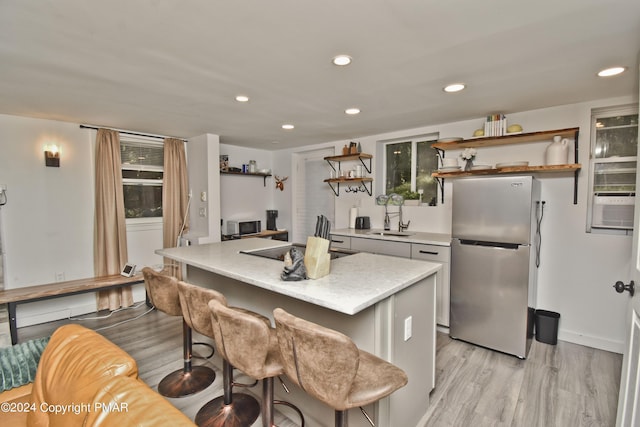 kitchen with a sink, light wood-style floors, freestanding refrigerator, a center island, and open shelves