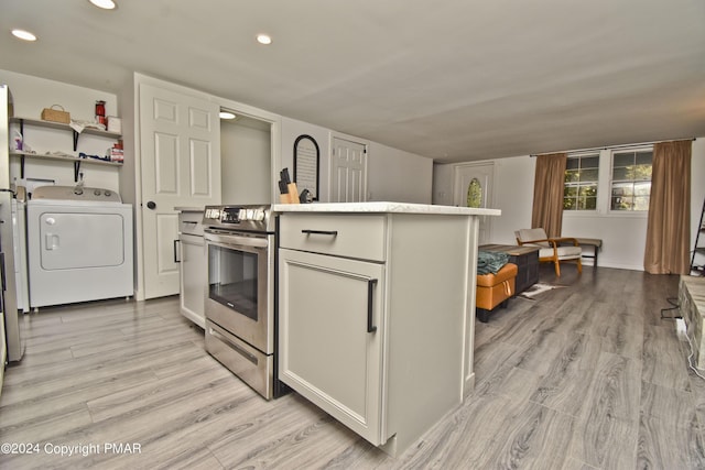 kitchen with a kitchen island with sink, recessed lighting, light wood-type flooring, stainless steel electric range, and washer / dryer