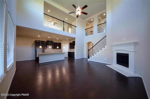 unfurnished living room featuring ceiling fan, baseboards, a fireplace with raised hearth, and dark wood-style flooring