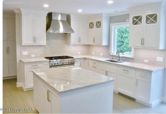 kitchen featuring a kitchen island, high end range, wall chimney range hood, white cabinetry, and a sink