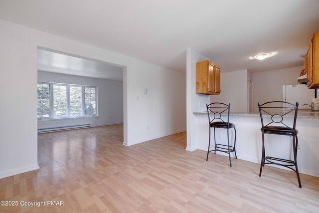 kitchen featuring a baseboard radiator, white fridge, a breakfast bar, and light wood-type flooring