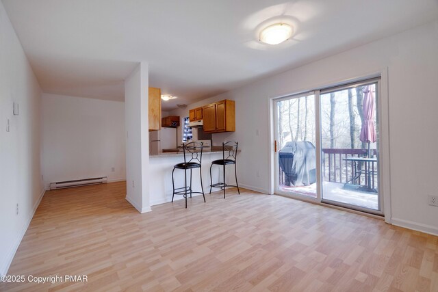 kitchen with a baseboard heating unit, a kitchen breakfast bar, white refrigerator, kitchen peninsula, and light wood-type flooring