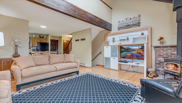 living area featuring a baseboard heating unit, light wood-style floors, a wood stove, beamed ceiling, and stairs