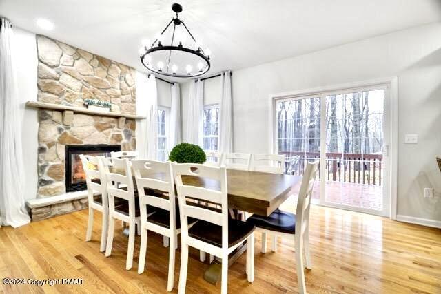 dining space with a chandelier, a stone fireplace, wood finished floors, and baseboards