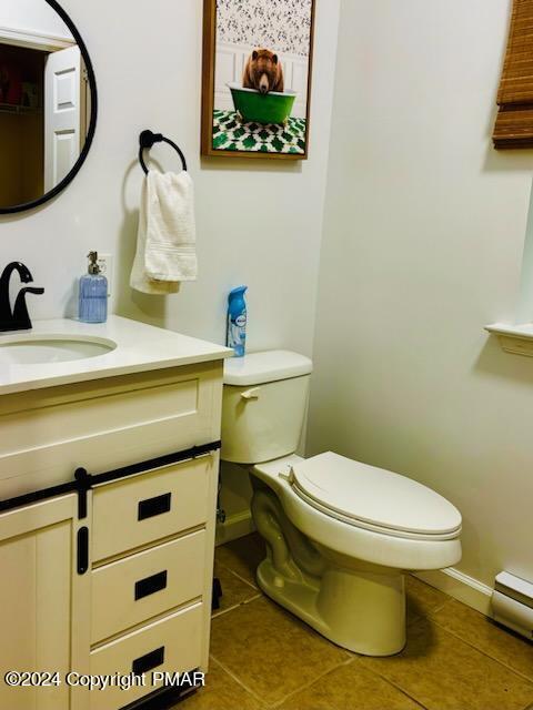 half bath featuring baseboards, toilet, tile patterned flooring, baseboard heating, and vanity